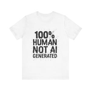 Op de afbeelding: Wit t-shirt met de tekst "100% HUMAN NOT AI GENERATED" in een glitch-stijl lettertype. De zwarte tekst heeft een digitaal printplaatontwerp. Het t-shirt heeft een ronde hals.