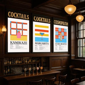 May include: Three framed cocktail posters with black borders are displayed on a dark wood wall. The posters feature colourful graphic designs and the names "Kamikaze," "Margarita," and "Cuba Mojito." The word "COCKTAILS" is at the top of the first two posters, and "COSMOPOLITAN" is at the top of the third.