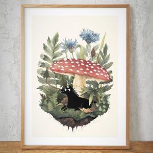 May include: A framed art print featuring a whimsical illustration. A black unicorn rests beneath a large red mushroom with white spots, surrounded by greenery and blue flowers. The artwork is set against a neutral background.