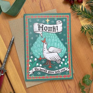 May include: Greeting card with a whimsical illustration of a goose with the word "Honk!" in a banner. The card has a green background with white flowers and the text "The herald goose doth sing."