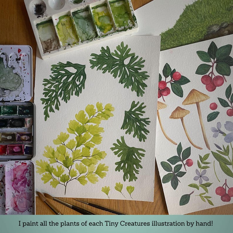 May include: Two sheets of watercolor paper featuring hand-painted botanical illustrations of green ferns, yellow foliage, brown mushrooms, red berries, and purple flowers, accompanied by watercolor paint palettes and brushes on a wooden surface.