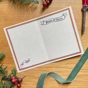 May include: Open greeting card with a festive red and green border. The card reads "Peace on Earth" in a banner and "honk" in a smaller banner. A green velvet ribbon and sprigs of berries and greenery are in the background.