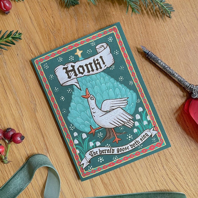 May include: A greeting card with a green background and a white goose illustration. The card reads "Honk!" in a banner and "The herald goose both sing" on a ribbon. A decorative pen rests beside the card.