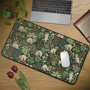 May include: A rectangular mouse mat with a cream-coloured cat design set against a dark green floral pattern with red and white details. The mat is on a wooden desk, with a laptop and mouse visible.