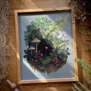 May include: A framed art print featuring a dark, fuzzy creature with glowing pink eyes sitting in a lush forest scene. The illustration includes green ferns, light purple flowers, small brown mushrooms, and red berries on a patch of mossy earth.