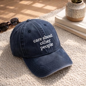 May include: A navy blue baseball cap with the embroidered text "care about other people" in white. The cap has a curved brim and a classic six-panel design. The hat is made of a soft, worn-in fabric.