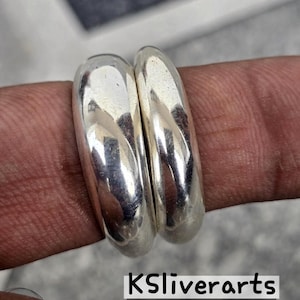 Op de afbeelding: Een close-up van twee gepolijste zilveren ringen. De ringen zijn glad en afgerond en reflecteren licht. De ringen zitten op een vinger. De tekst "KSliverarts" staat onderaan de afbeelding.