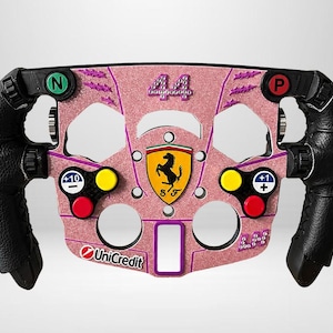 Könnte beinhalten: Ein rosafarbenes Glitzer-Rennlenkrad mit schwarzen Ledergriffen, verziert mit der Zahl 44 aus Strasssteinen, einem Ferrari-Logo und Tasten mit der Beschriftung N, P, +10 und +1. Das UniCredit-Logo ist unten links aufgedruckt, mit LH aus Strass.