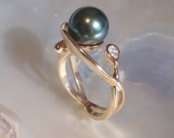May include: A gold ring with a black pearl and a small diamond accent. The ring has a unique, organic design.