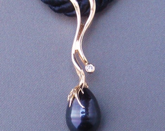Puede incluir: Un collar con un colgante de oro, una perla negra y un pequeño diamante. El colgante tiene forma de rama con una perla en el extremo.