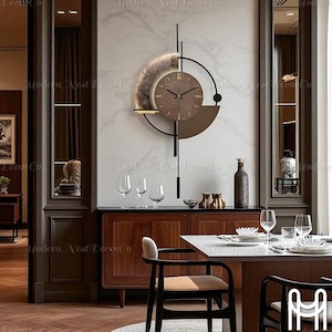 Könnte beinhalten: Eine moderne Wanduhr mit braunem Zifferblatt und schwarzen Zeigern, vor einer weißen Wand mit Marmoreffekt. Die Uhr hat ein einzigartiges Design mit einem kreisförmigen Element und einem Regal. Die Worte "Modern Nest Decor Co" sind sichtbar.
