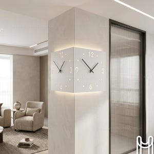 May include: A white corner wall clock featuring two faces that wrap around the wall edge. Each face displays black clock hands, gold-colored numerals at 12, 3, 6, and 9, and dot markers for other hours. The clock includes integrated backlighting.