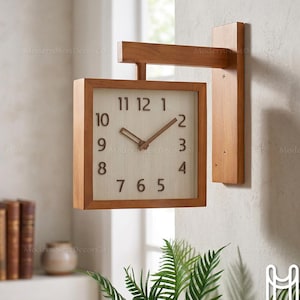 May include: A square wall-mounted clock with a light brown wooden frame and a matching wooden arm extending from a vertical wall plate. The clock face is off-white with dark brown numerals from 1 to 12 and two matching dark brown clock hands.