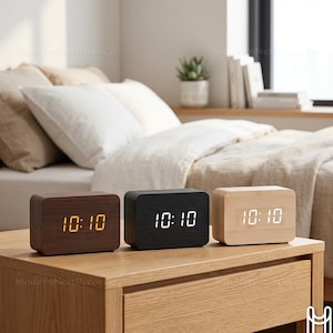 Puede incluir: Tres relojes despertadores digitales rectangulares de madera en tonos marrón, negro y madera clara, cada uno mostrando la hora 10:10. Los relojes están sobre una mesita de noche de madera. Los relojes son un artículo de decoración moderno.