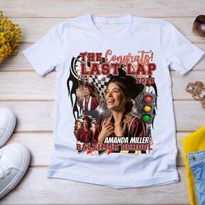 May include: White t-shirt with a graphic design featuring a woman, the text "The Congrats! Last Lap 2026", and the name "Amanda Miller, Baltimor School". The design includes a checkered flag and a traffic light.