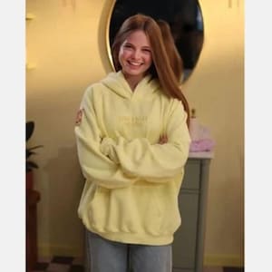 May include: A pale yellow hoodie with the text "Sincerely Young" in yellow. The hoodie features a hood and long sleeves. The person in the image is wearing blue jeans.