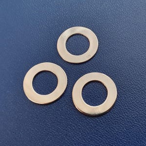 Può includere: Tre componenti metallici circolari color oro rosa lucido, con un foro al centro. Il metallo ha una superficie liscia e riflettente. Un componente ha il numero "925" stampigliato. Sono disposti su una superficie blu scuro.