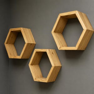 May include: Three hexagonal wall shelves crafted from light-toned wood with a visible grain pattern. The shelves are arranged in a cluster, featuring open centers and flat surfaces for storage, showcasing a natural finish and geometric construction.