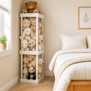 May include: A white wooden vertical storage unit with two tiers, featuring thin vertical bars that hold a collection of plush stuffed animals, including various teddy bears, rabbits, and a panda, with a large brown teddy bear sitting on top.