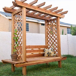 May include: A wooden pergola with a bench, featuring a lattice design on the sides and a slatted roof. A small potted plant sits on the bench's side. A decorative pillow with yellow and black patterns rests on the bench.