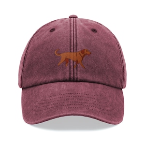 Op de afbeelding: Een bordeauxrode baseballcap met een gebogen klep. De cap heeft een bruin geborduurd beeld van een hond op de voorkant. De cap heeft een ontwerp met zes panelen, een knoop bovenop en een verstelbare band.