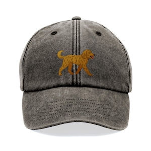 May include: A charcoal gray baseball cap with a distressed finish. The cap features an embroidered golden retriever dog in a walking pose. The dog has a light brown coat and a pink tongue. The cap has a curved brim and an adjustable strap.