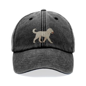 Könnte beinhalten: Dunkelgraue Baseballkappe mit einer gestickten Illustration eines hellbeigen Hundes. Der Hund hat die Zunge draußen. Die Kappe hat einen gebogenen Schirm und einen verstellbaren Riemen.