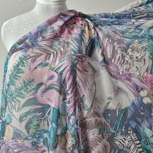 Könnte beinhalten: Transparenter Stoff mit einem lebendigen tropischen Druck, der rosa Flamingos, Zebras und üppiges Laub in Grün-, Lila- und Rosatönen zeigt. Das Design umfasst Illustrationen von Schmetterlingen, Blumen und anderen Wildtieren. Der Stoff ist über einer Schaufensterpuppe drapiert.