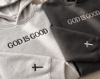 Op de afbeelding: Een lichtgrijze hoodie en een donker antracietgrijze hoodie, beide voorzien van de geborduurde tekst GOD IS GOOD op de borst en een klein geborduurd kruis op de mouwboord. Elke hoodie heeft lange mouwen met geribbelde boorden.