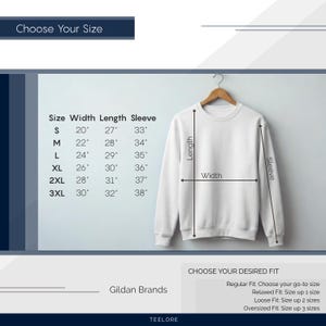 May include: White crewneck sweatshirt displayed on a wooden hanger. Size chart shows measurements in inches for width, length, and sleeve length. Text includes "Choose Your Size" and "Choose Your Desired Fit". The brand is Gildan.