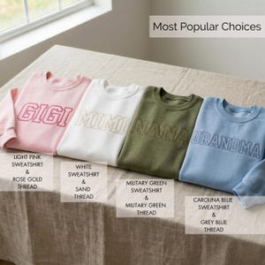 Op de afbeelding: Vier crewneck sweatshirts in lichtroze, wit, legergroen en lichtblauw. Elk sweatshirt heeft een geborduurde naam: GIGI, MIMI, NANA en GRANDMA. Het roze sweatshirt heeft ros&eacute;goud draad, het witte heeft zanddraad, het groene heeft groen draad en het blauwe heeft grijsblauw draad.