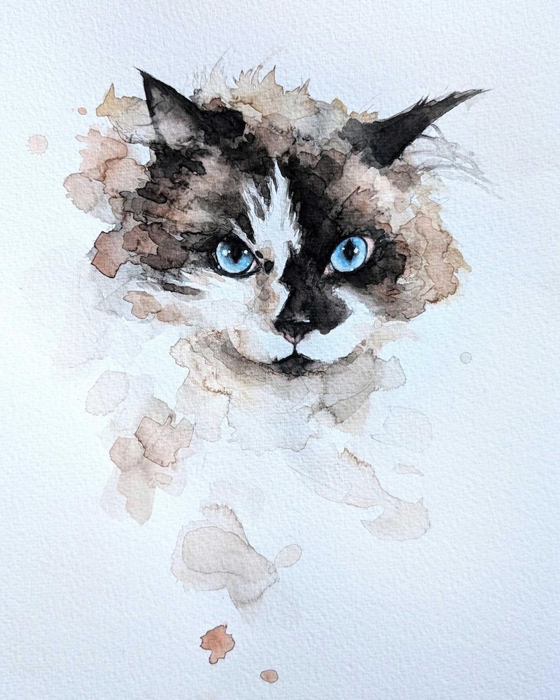May include: Watercolor painting of a cat's face with striking blue eyes. The cat has a black and white face with brown and tan fur. The artwork has a soft, watercolor style with brown and tan paint splatters around the cat's face.