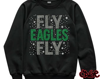 May include: Black sweatshirt with the text "FLY EAGLES FLY" in silver and green rhinestone-like letters. The design includes small white dots, and the sweatshirt has a crew neck and long sleeves.