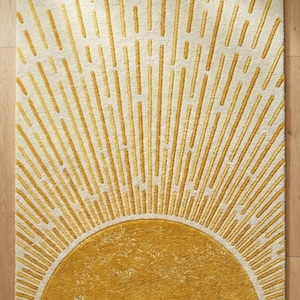 Puede incluir: Una alfombra rectangular con un diseño de rayos de sol. La alfombra presenta un fondo color crema con un gran sol semicircular en un tono amarillo dorado en la parte inferior. Líneas amarillo dorado irradian hacia arriba, creando un efecto visual llamativo.