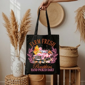 Könnte beinhalten: Schwarze Tragetasche mit einem rosa Oldtimer-Truck, der Kürbisse transportiert, umrahmt von einem rosa Blumenkranz. Der Text "FARM FRESH" und "Pumpkins HAND PICKED DAILY" ist auf der Tasche aufgedruckt.