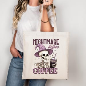 Könnte beinhalten: Cremefarbene Tragetasche mit einem lila Motiv eines Skeletts mit Hexenhut und Kaffeetasse. Der Text "NIGHTMARE before COFFEE" ist lila gedruckt. Die Tasche hat lange, cremefarbene Henkel.