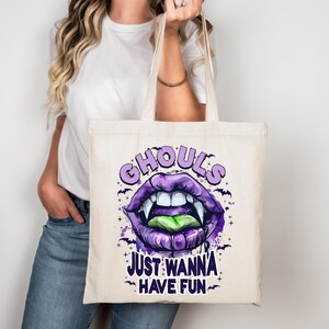 May include: A cream tote bag with a purple and green vampire lips graphic and the text "Ghouls Just Wanna Have Fun." The design includes bats and stars. The bag has two handles.