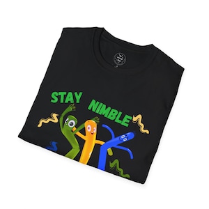 Può includere: T-shirt nera con la scritta verde "STAY NIMBLE" e un'illustrazione a cartoni animati di tre uomini tubo gonfiabili colorati. Gli uomini tubo sono verdi, arancioni e blu con linee ondulate.