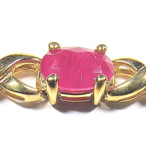 May include: A gold-toned bracelet featuring an oval-cut, vibrant pink gemstone set in a four-prong mounting. The band is composed of interlocking, twisted metal links that create a continuous, woven pattern along the length of the jewellery piece.