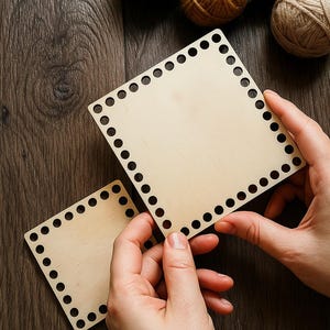 May include: Two square wooden bases with evenly spaced holes around the perimeter, ideal for crafting. The bases are held by hands, with several balls of yarn in shades of green, yellow, and red in the background. The wood has a natural, light color.