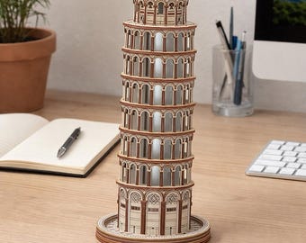 May include: A wooden model of the Leaning Tower of Pisa. The model is made of light brown wood with detailed architectural features, including arched windows and decorative trim. The tower stands on a circular base and is displayed on a wooden desk.