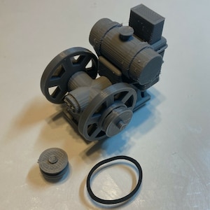 May include: A gray 3D printed model of a small engine with a belt and pulley system. The engine has a fuel tank, a cylinder, and a crankshaft. The model is sitting on a white surface.