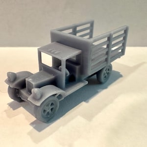 May include: A gray toy truck with a detailed design. The truck features a cab with a roof, a cargo bed with slatted sides, and four wheels. The headlights are round, and the truck appears to be a vintage model.