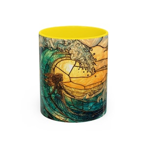 May include: A ceramic mug with a stained-glass design featuring a mermaid and a large ocean wave. The wave is depicted in shades of green and gold, with the mermaid in the foreground. The interior of the mug is bright yellow.