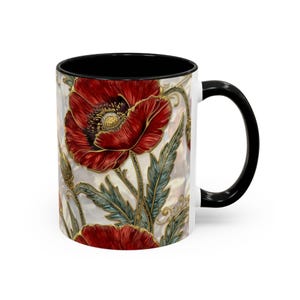 May include: White ceramic mug with a black interior and handle. The mug features a detailed illustration of red poppies with green leaves and gold accents. The design wraps around the mug.