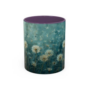 Könnte beinhalten: Eine Keramik-Tasse mit einem teal- und lila-farbenen Design. Die Außenseite zeigt ein Gemälde von Löwenzahnpflanzen mit weißen Samenköpfen vor einem teal-farbenen Hintergrund. Die Innenseite der Tasse ist lila.