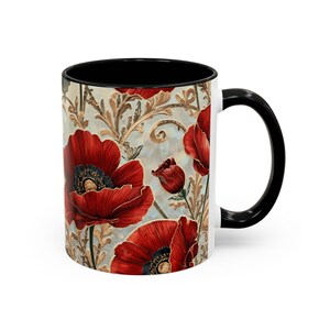 May include: A ceramic coffee mug with a black interior and handle, featuring a vibrant floral design. The design showcases large red poppies with black centers against a light blue background with gold accents. The mug is white on the exterior.