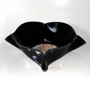 May include: A black, upcycled vinyl record bowl. The bowl is shaped with curved edges and a central circular base, showcasing the original record label. The bowl's design is a unique, eco-friendly decorative piece.