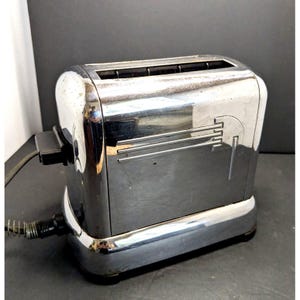May include: A chrome-plated two-slice toaster with a polished reflective finish. The appliance features horizontal embossed lines on the side panel, a black power cord with a spring-reinforced strain relief, and a black electrical plug attached.