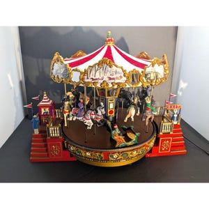 May include: A miniature carousel with a red and white striped canopy, gold trim, and painted winter scenes. The ride features various horses and figures on a circular platform, flanked by two red staircases with an exit sign and small figurines.